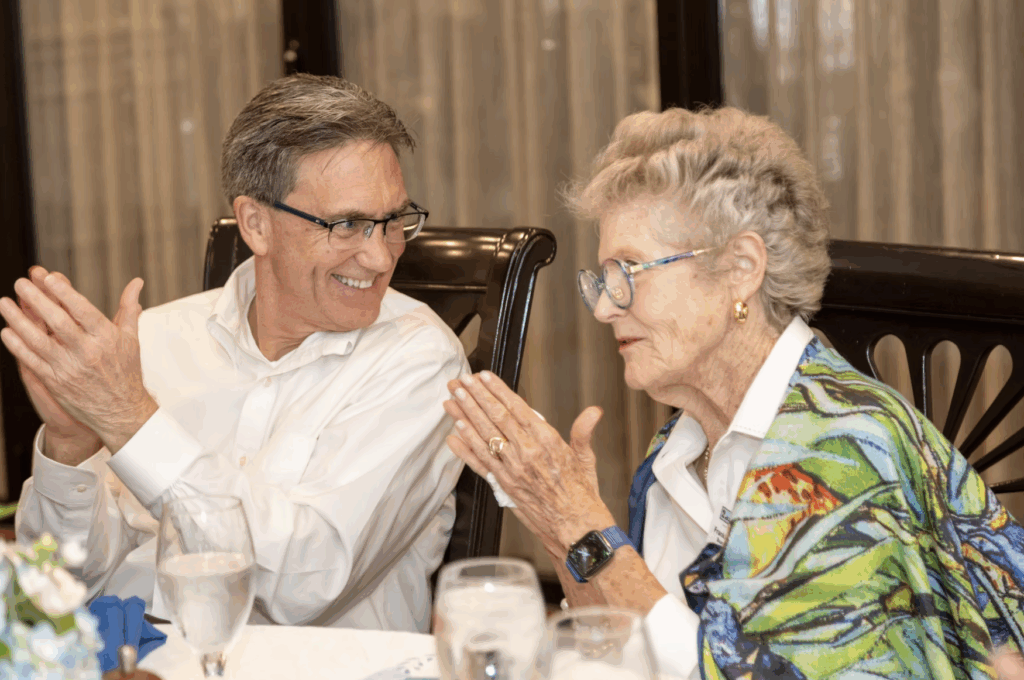A man sitting at a table looks at the woman beside him as both clap