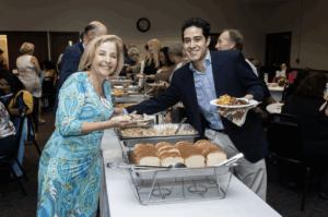 Dressed up man and woman on either side of a buffet pause to smile for the camera