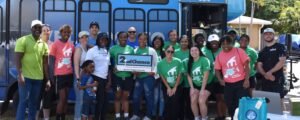A group of volunteers in green and pink tshirts hold a 2nd Chance sign in front of a blue bus